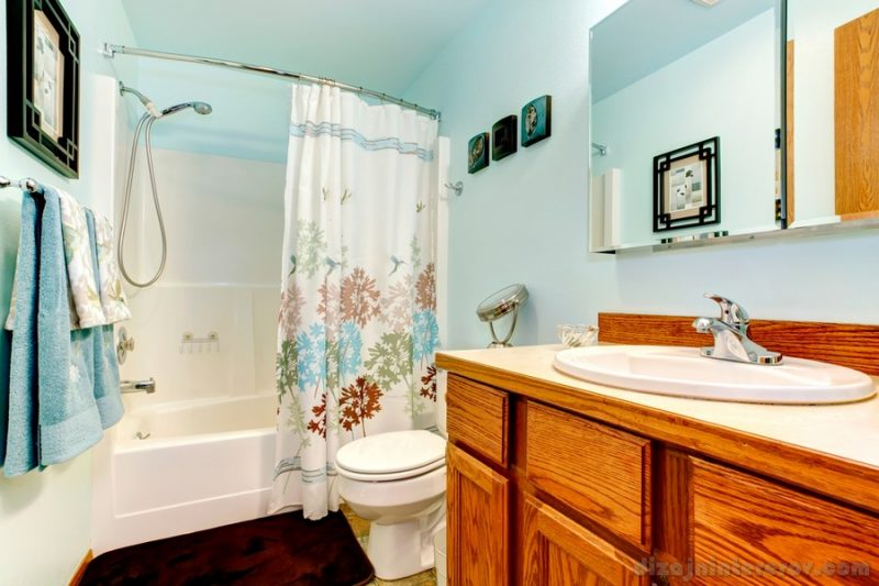 Light blue bathroom with wood cabinets. tile floor. Decorated with bluee and white towels and curtains