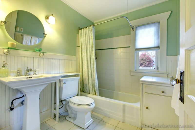 Mint bathroom with light green curtains, tile floor and wood plank wall trim. View of sink, toilet and bath tub