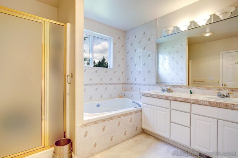 Bright bathroom with window. View of tile wall trim, bath tub, cabinets and glass door shower
