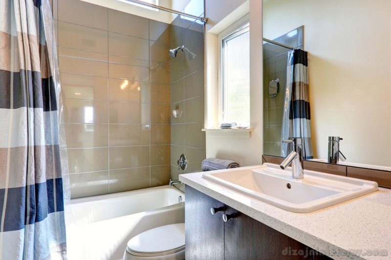 Small bathroom with window. View of washbasin cabinet with mirror and tub with tile wall trim