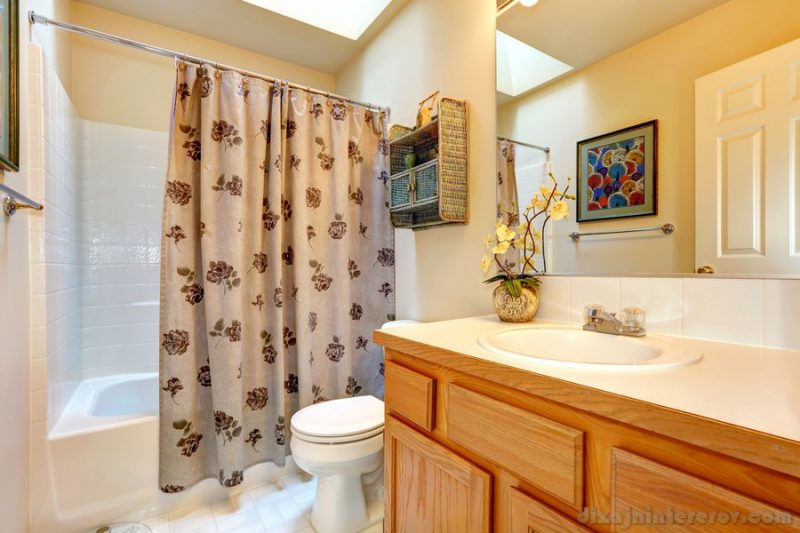 Soft colors bathroom with honey tone bathroom vanity cabinet, large mirror. View of bath rub with curtains
