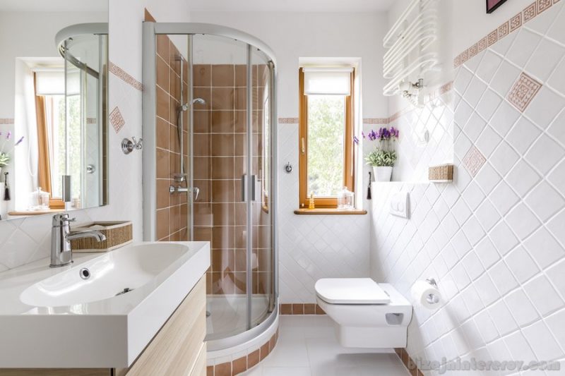 Glass shower in small white bathroom with sink, mirror and toilet